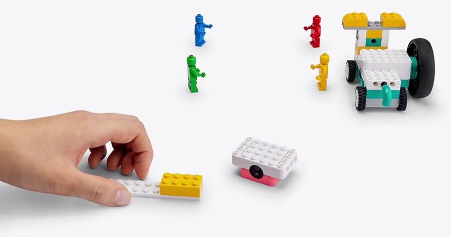 Una mano acerca una pieza de color al sensor mientras un vehículo LEGO con motor espera